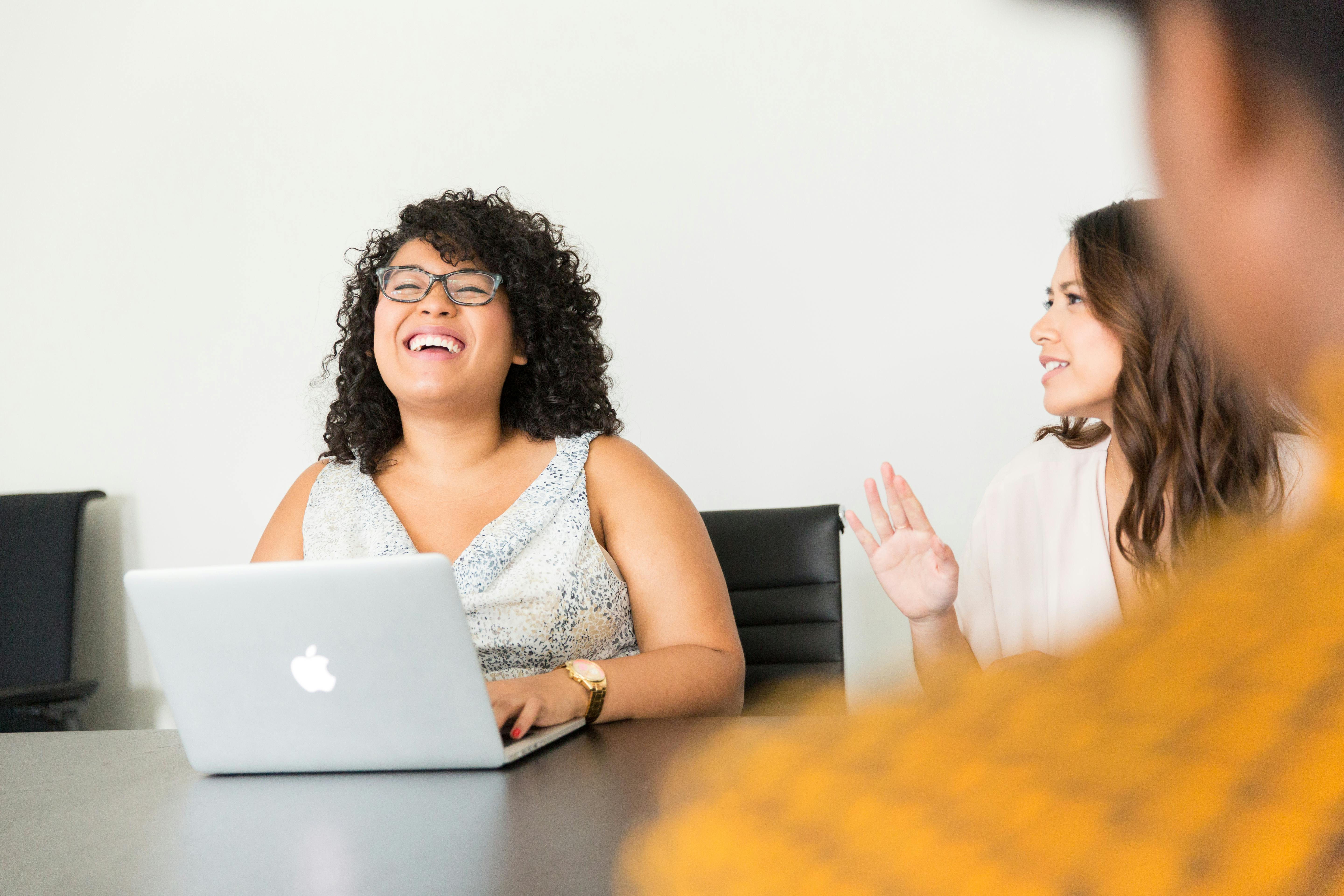 A photo of three professionals working together at a table with a laptop open. One is laughing.